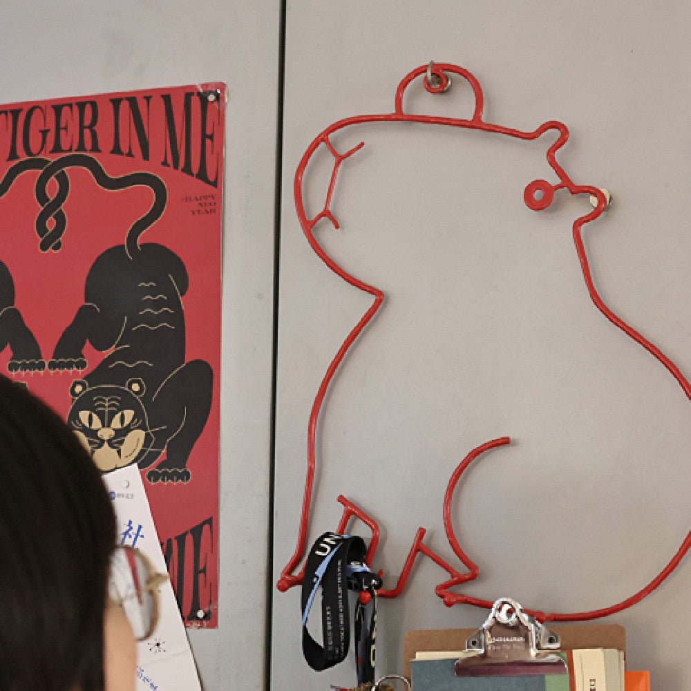 Red wire wall art of a face on a gray wall with a poster in the background.