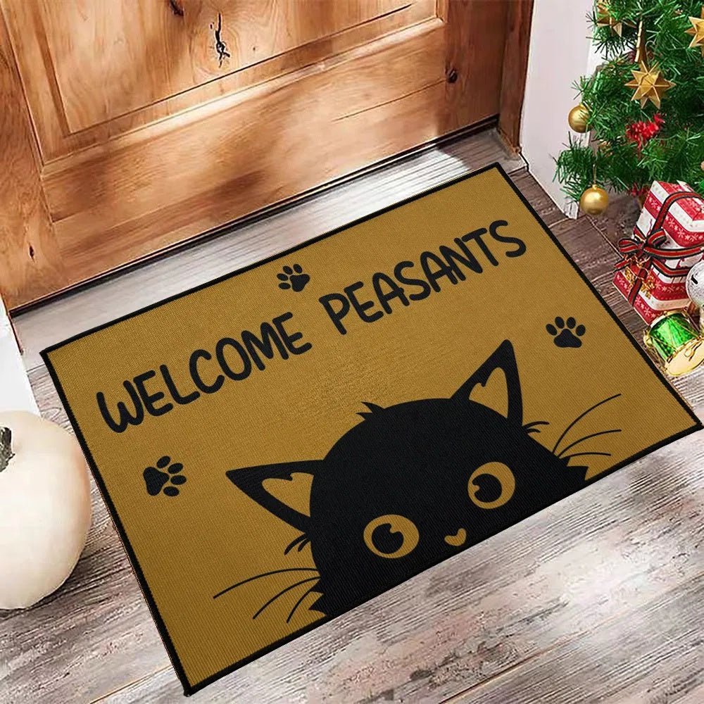 Doormat with a black cat design and 'Welcome Peasants' text on a wooden floor.