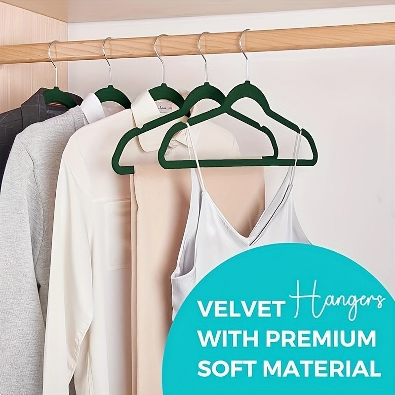 Green velvet hangers with clothes on a wooden rack against a white wall.
