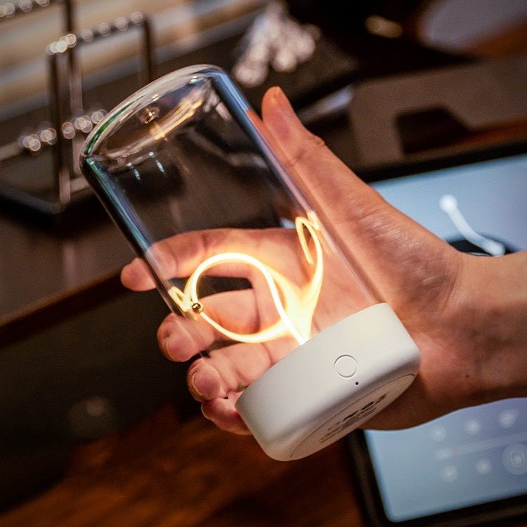 Hand holding a transparent container with glowing interior, connected to a white device, in a kitchen setting.