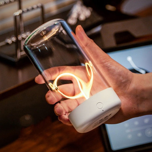 Hand holding a transparent container with glowing interior, connected to a white device, in a kitchen setting.