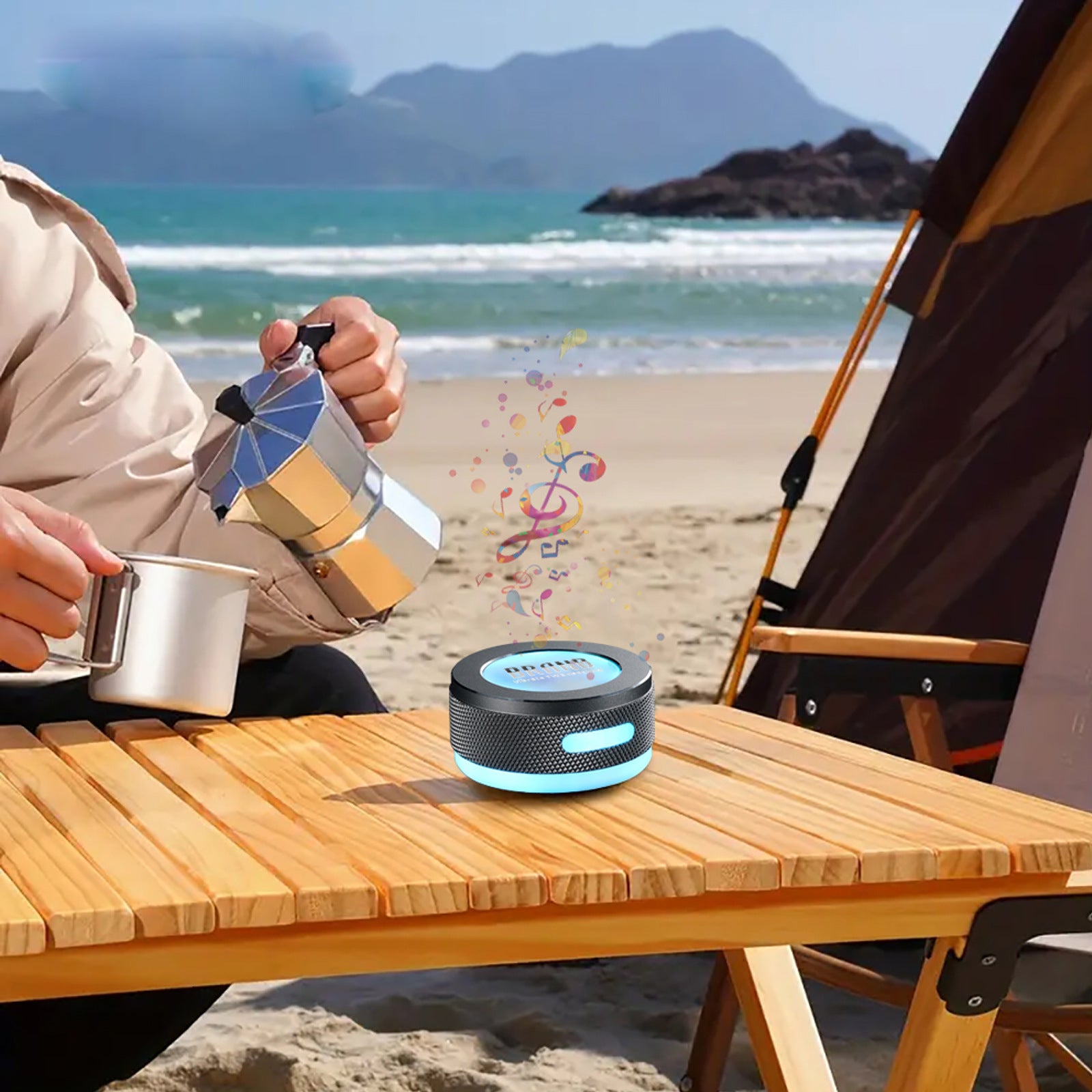Person making coffee on a beach with a coffee percolator and a portable speaker.