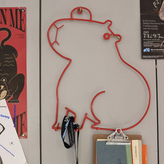 Red wire wall hook shaped like a person with items attached on a gray wall.