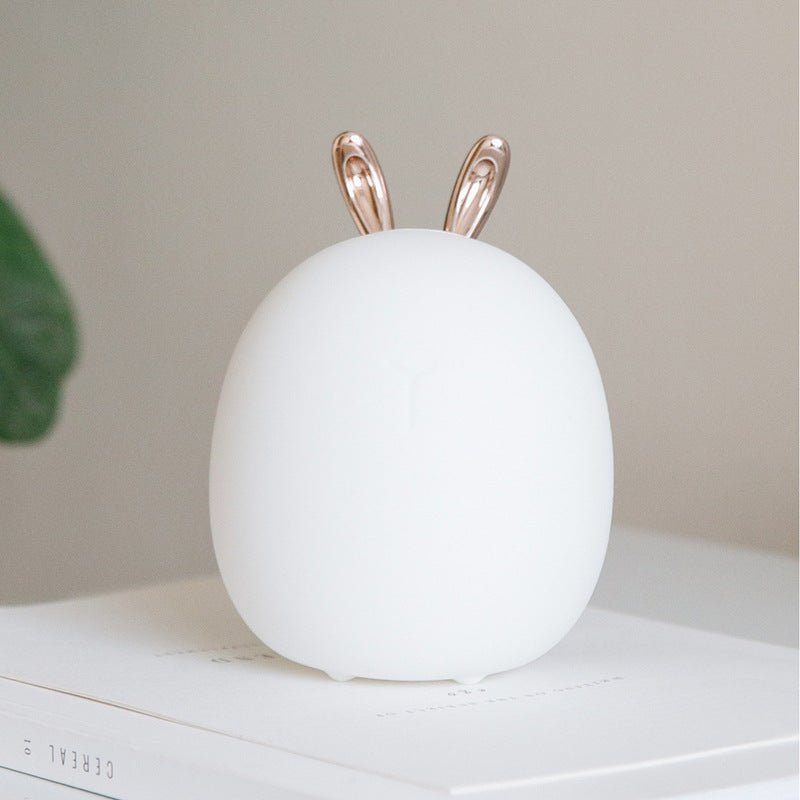 White egg-shaped night light with rose gold bunny ears on a white surface.