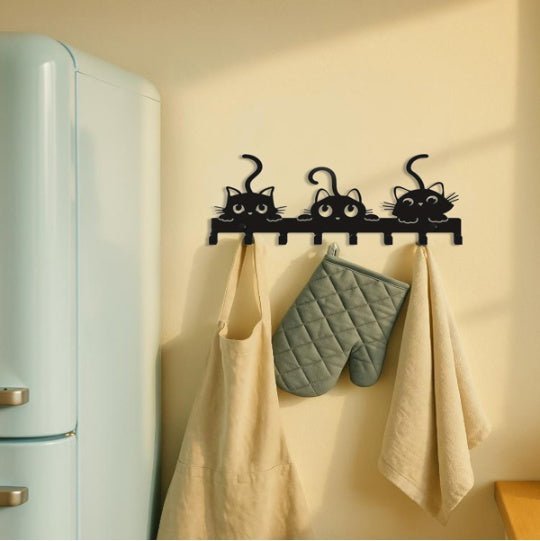 Wall-mounted hook with cat designs holding towels and an oven mitt next to a vintage-style refrigerator.