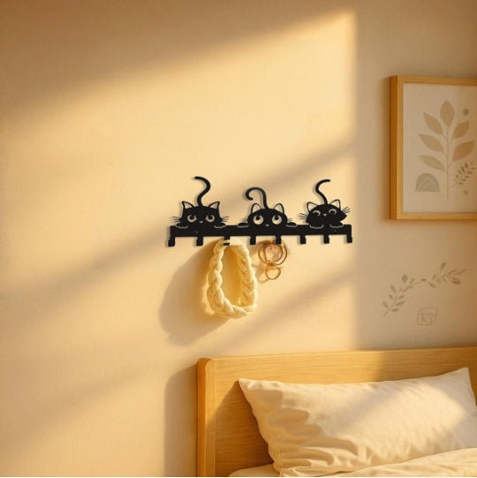 Decorative wall hook shaped like black cats on a beige wall above a bed.