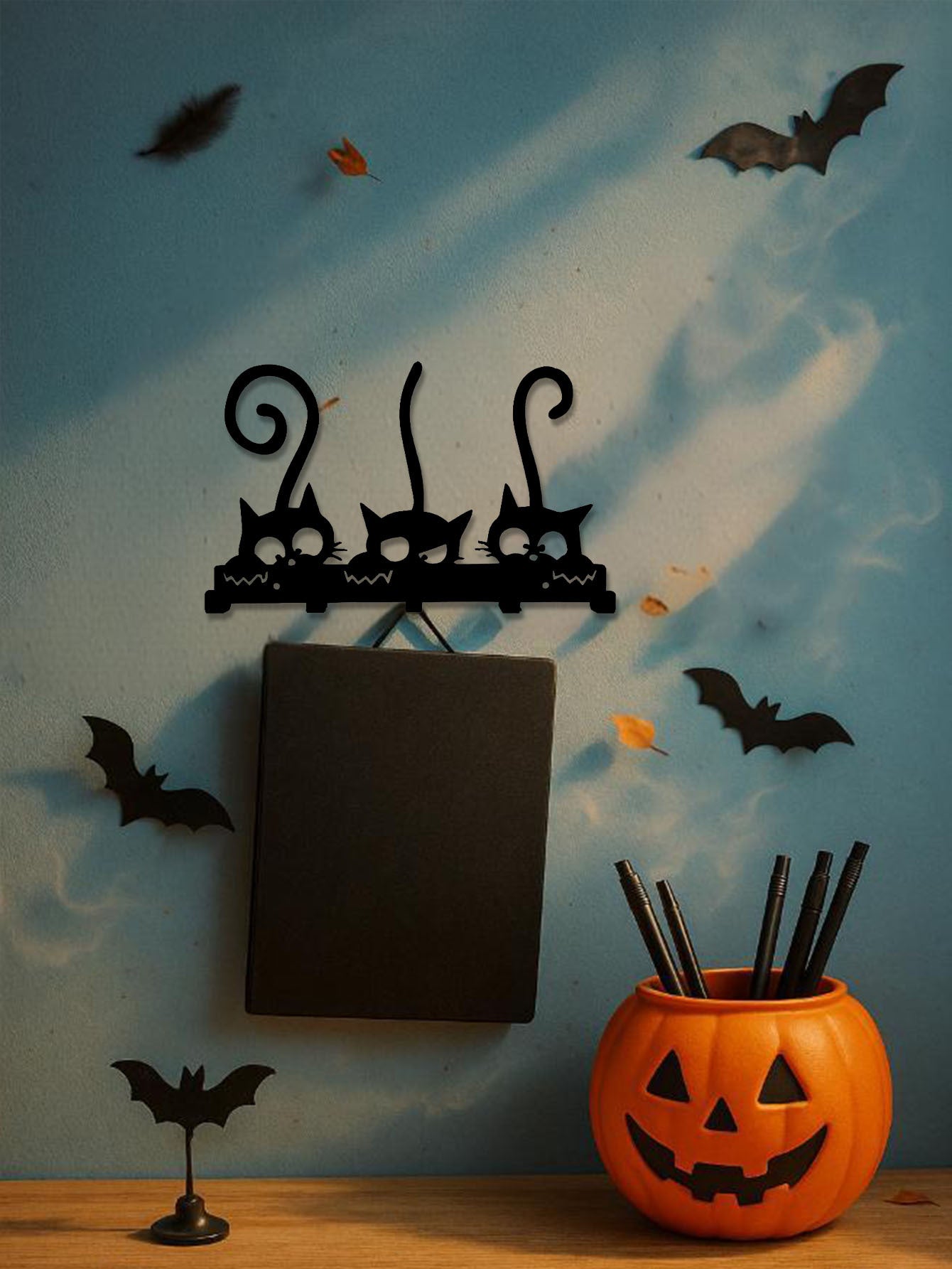 Halloween-themed decor with black cat hooks, pumpkins, and bats on a blue wall.