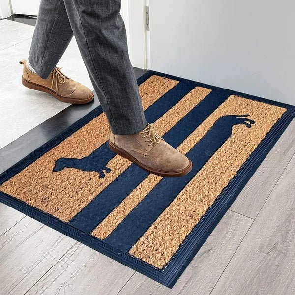 Person stepping onto a doormat with a brand logo, wearing brown shoes.
