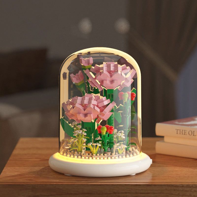 Decorative lamp with pink flowers and green plants inside a glass dome on a wooden surface.