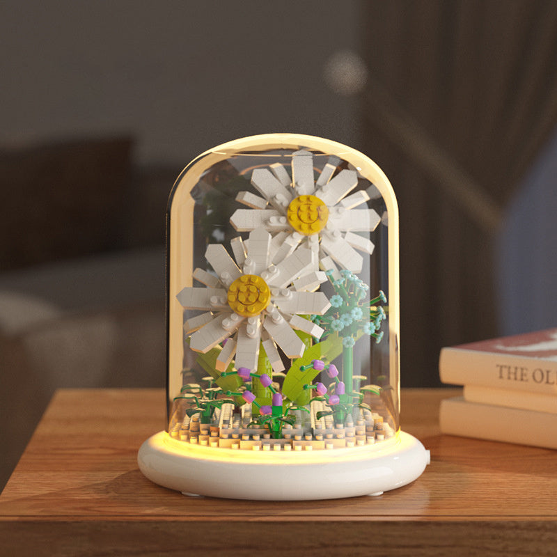 Decorative lamp with daisy flowers inside a glass dome on a wooden surface.