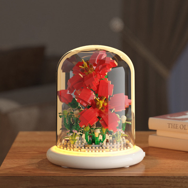 Decorative lamp with red flower and small figures inside a glass dome on a wooden surface.