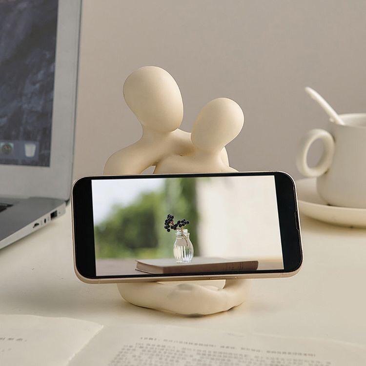 Phone stand with a phone displaying a scenic image on a desk with a laptop and mug in the background.
