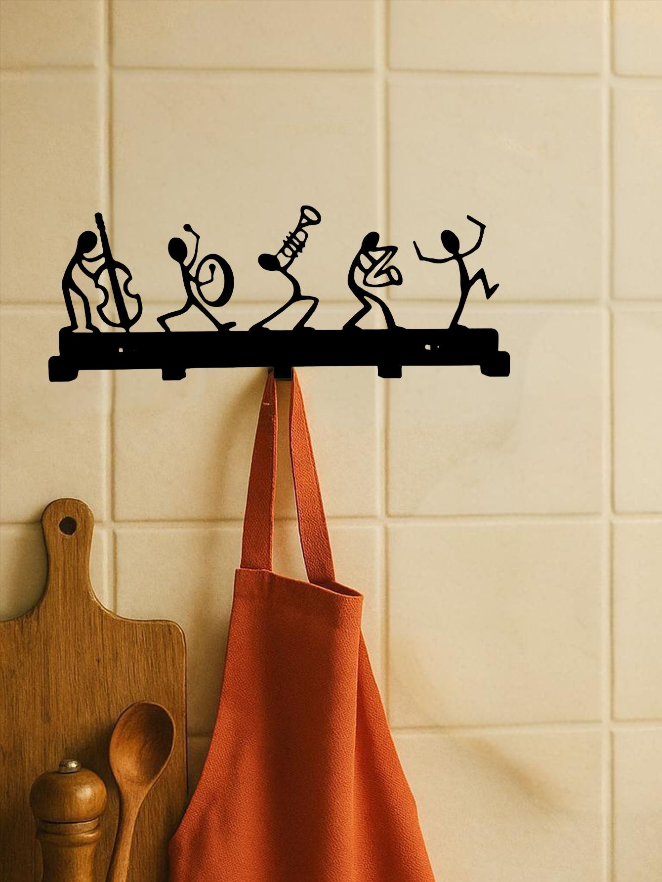 Decorative wall hook with black metal figures on a tiled wall with an orange apron hanging from it.