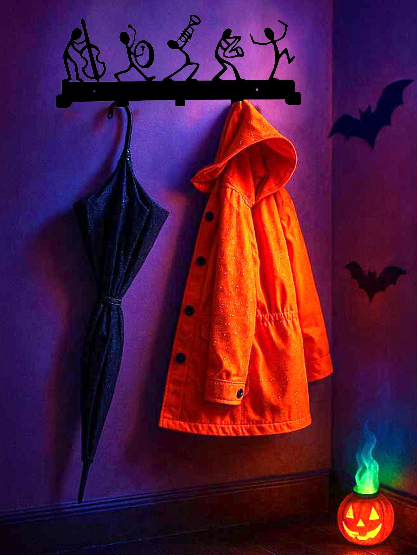 Halloween-themed coat rack with orange coat, black umbrella, and small pumpkin lantern on a purple wall.