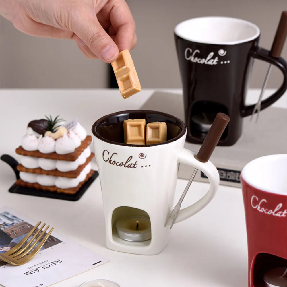 Person adding chocolate pieces to a 'Chocolat' mug with a candle, surrounded by other mugs and a dessert.