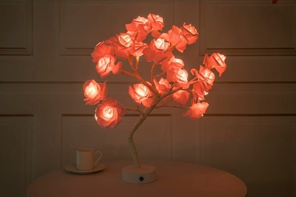 Decorative lamp shaped like a tree with glowing red flowers on a wooden surface.