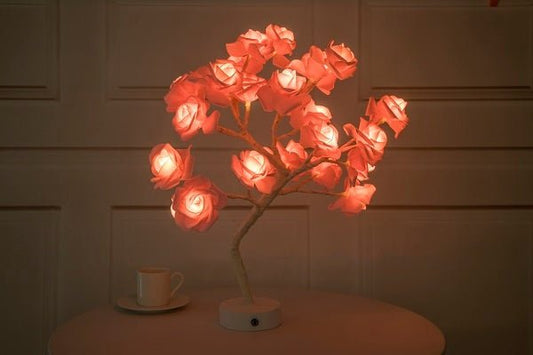 Decorative lamp shaped like a tree with glowing red flowers on a wooden surface.