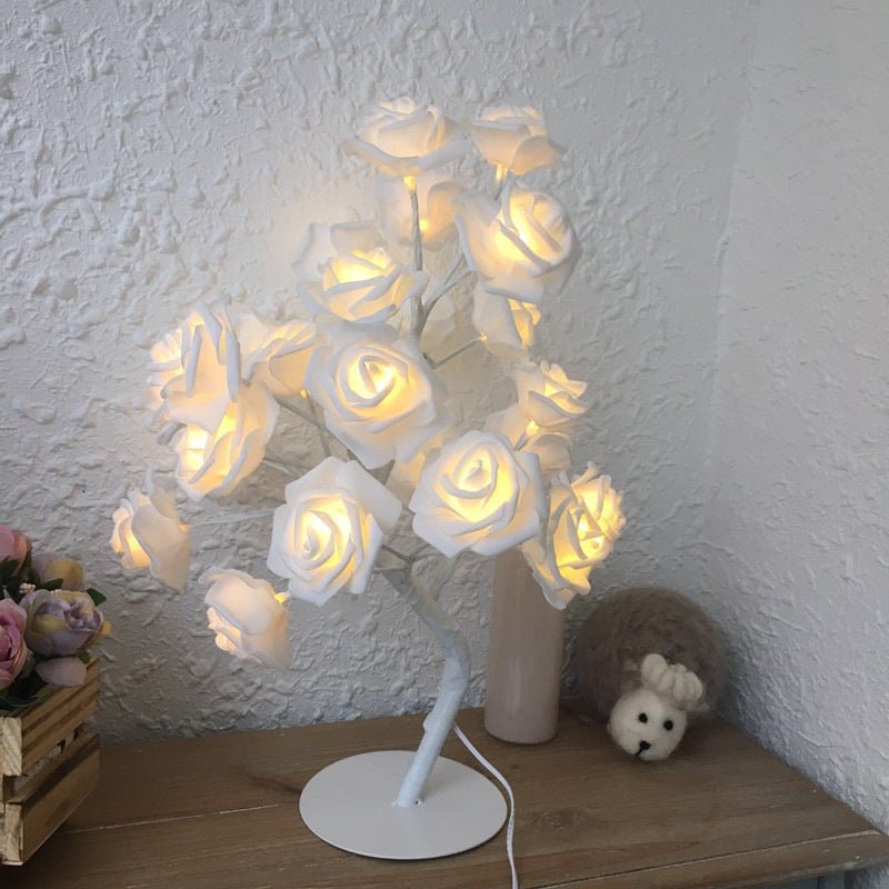 Decorative lamp with white roses on a wooden surface against a textured white wall.