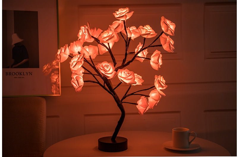 Decorative LED lamp shaped like a tree with illuminated pink flowers on a table.