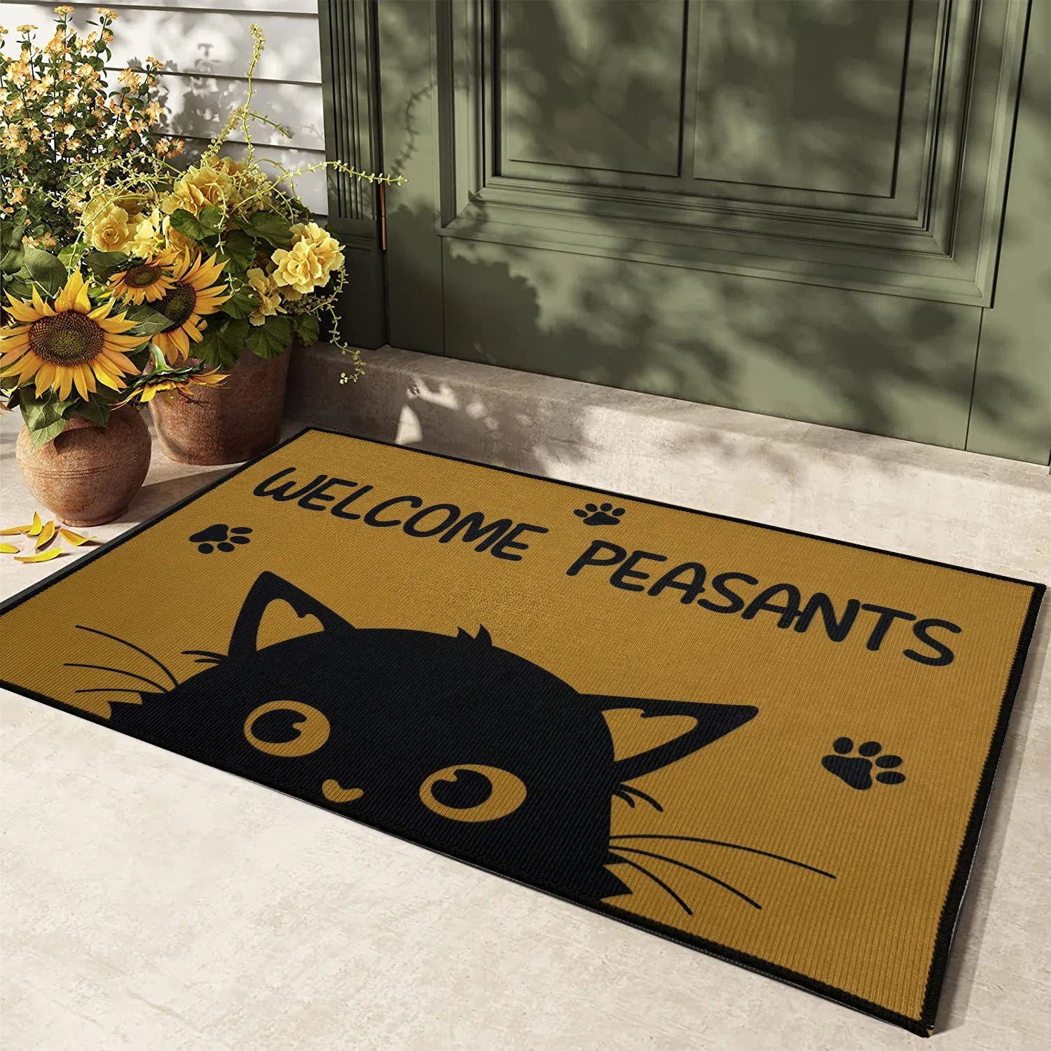 Doormat with a black cat design and 'Welcome Peasants' text, placed on a floor with flowers in the background.