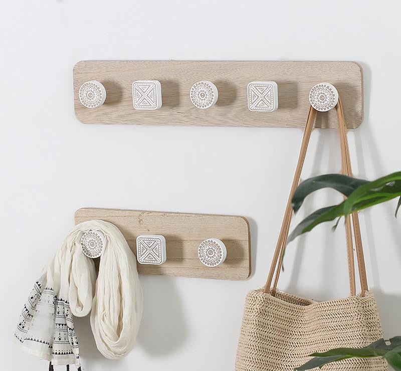 Wooden wall hooks with decorative knobs on a white wall, holding a scarf and a bag.
