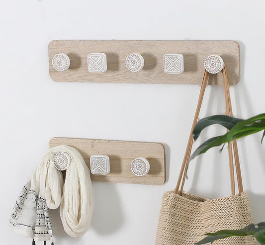 Wooden wall hooks with decorative knobs on a white wall, holding a scarf and a bag.