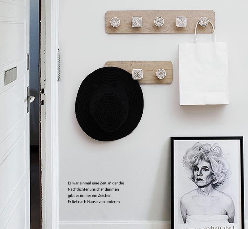 Wooden hook rack with a black hat and white bag on a white wall with text and a framed picture.